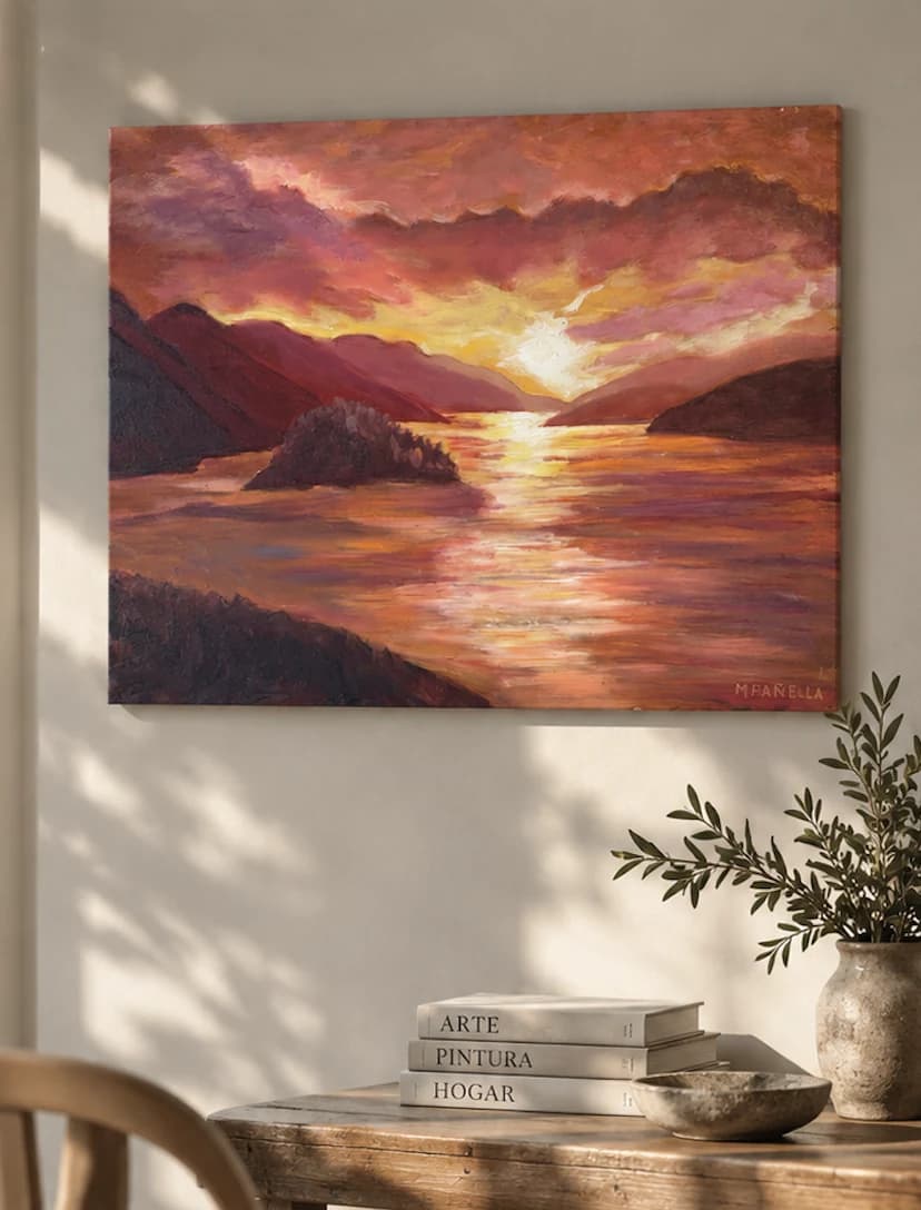 Óleo de Marina de un atardecer sobre el agua entre montañas, colgado en una pared clara junto a una mesa de madera con libros y una rama de olivo